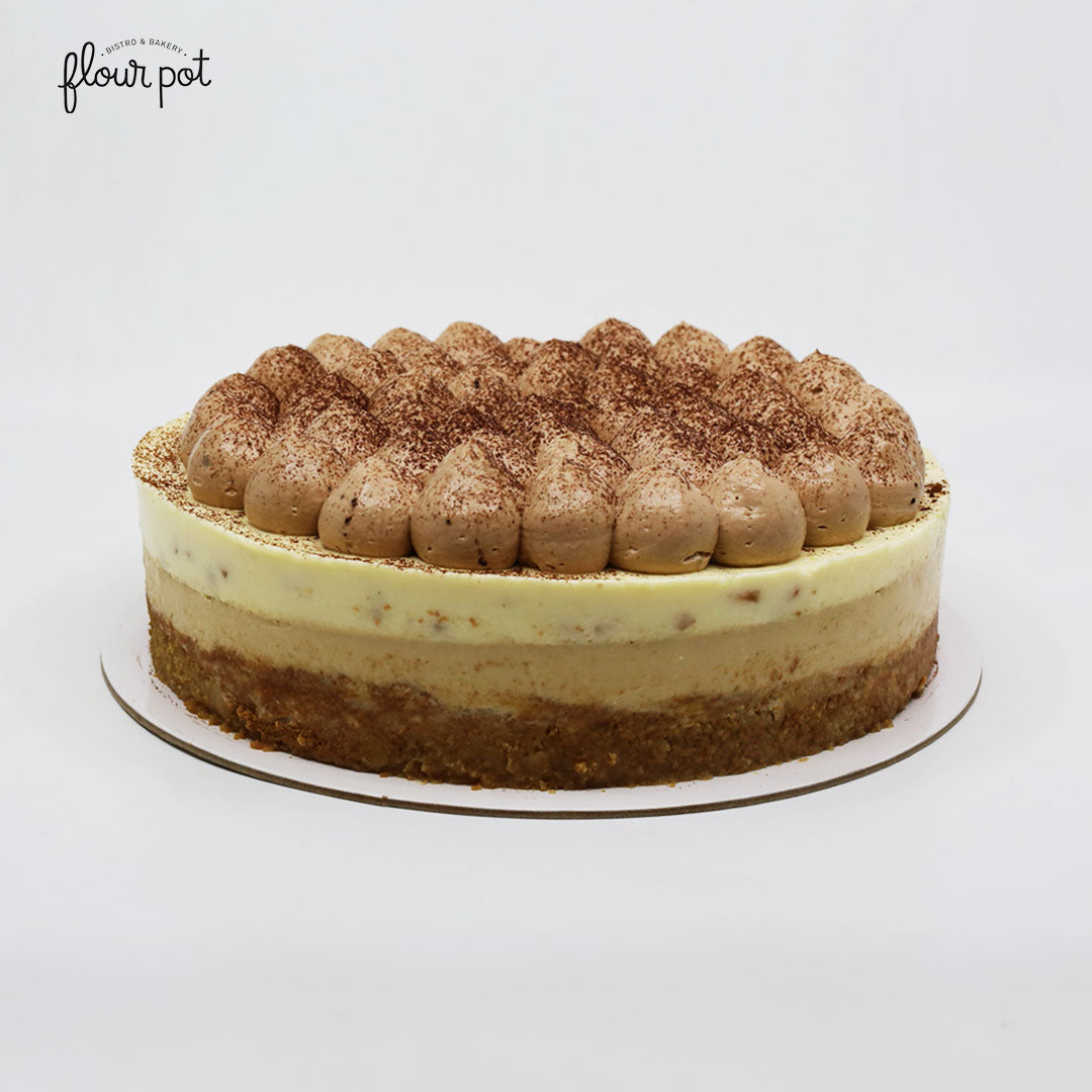 Layered banana fromage cake with a creamy mousse center, biscuit crust, and piped chocolate cream topping dusted with cocoa