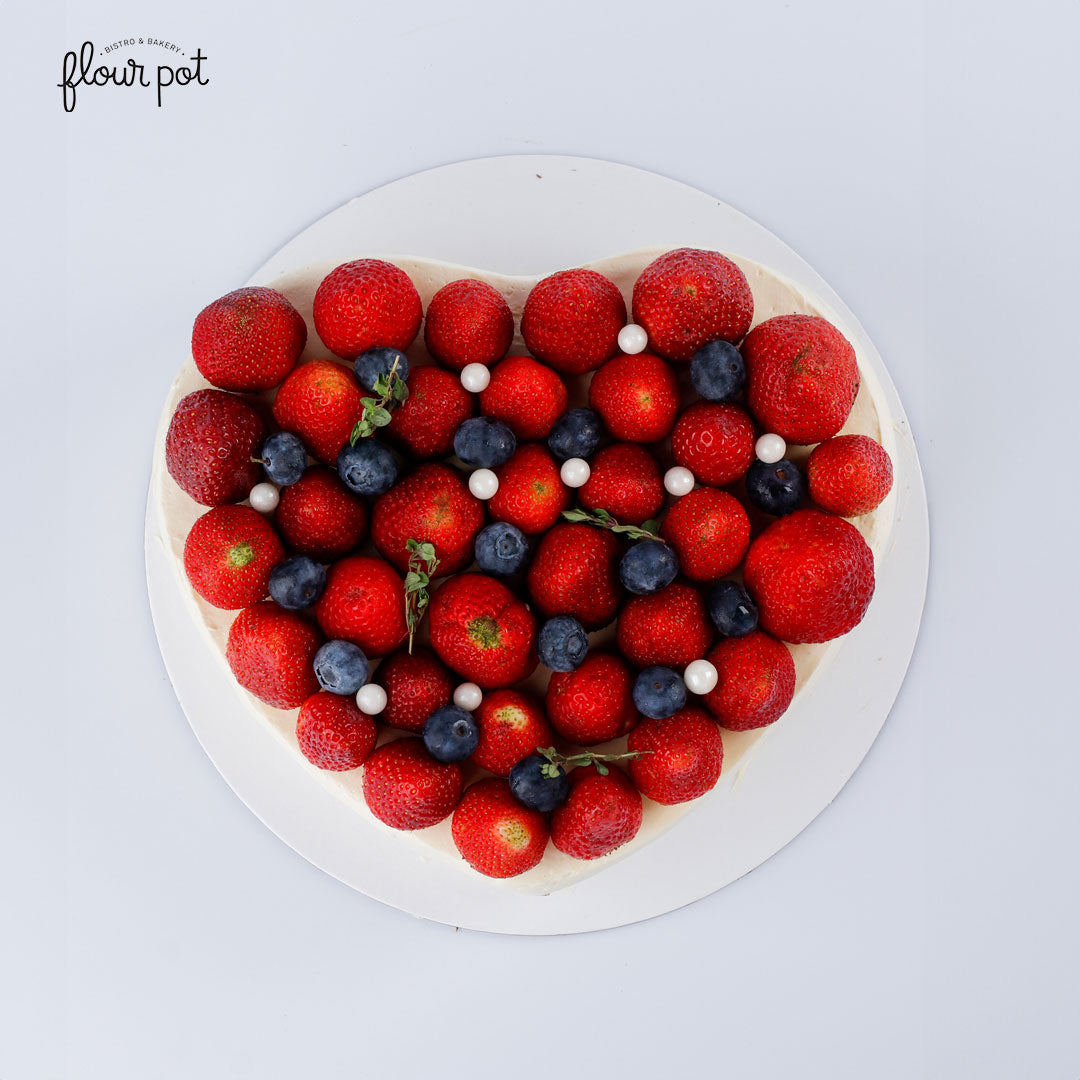 Heart-shaped pistachio cake topped with fresh strawberries, blueberries, edible pearls, and herbs