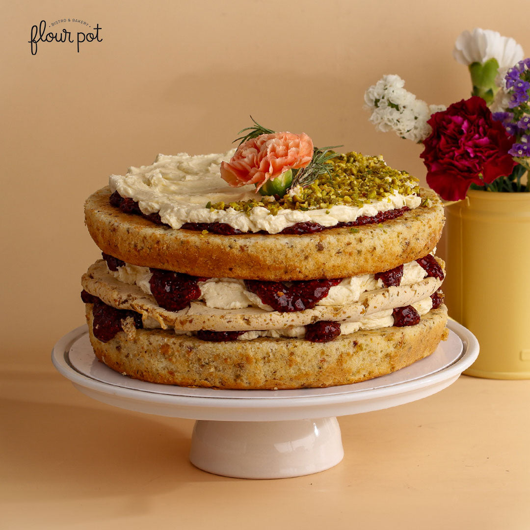 Rustic layered pistachio and berry cake topped with crushed pistachios, cream, and a fresh carnation flower