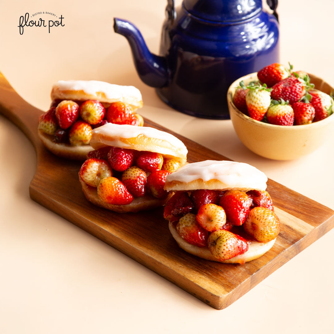 Strawberry-filled donuts topped with sugar glaze, served on a wooden board beside a bowl of fresh strawberries