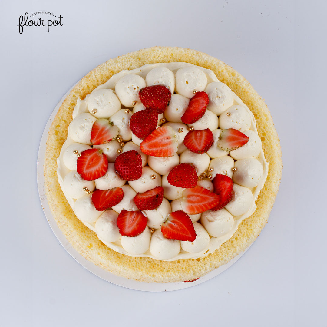 Strawberries and cream sponge cake topped with whipped frosting, fresh strawberries, and gold sugar pearls