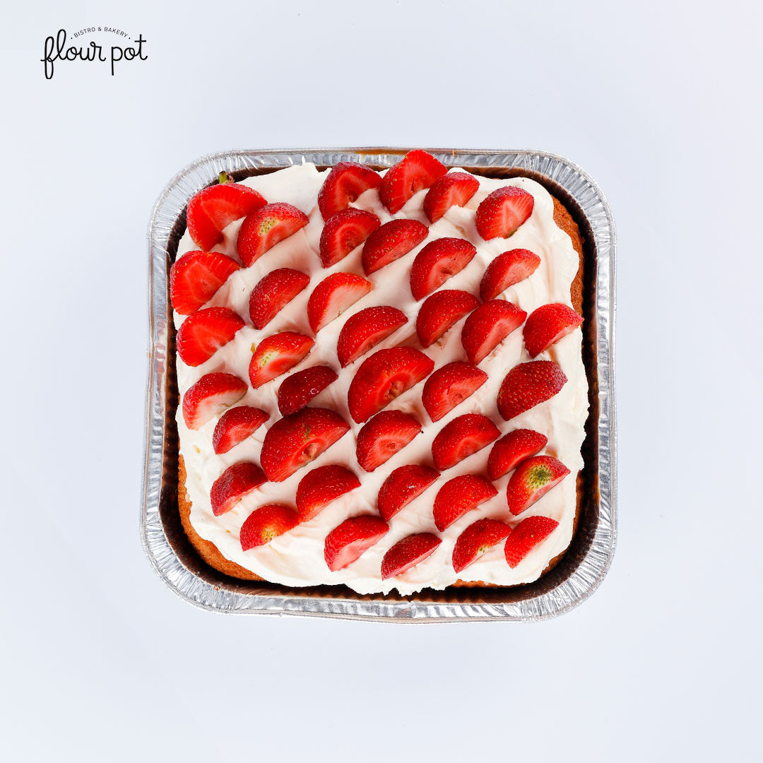 Strawberries tres leches cake topped with whipped cream and fresh strawberry halves, served in a tray