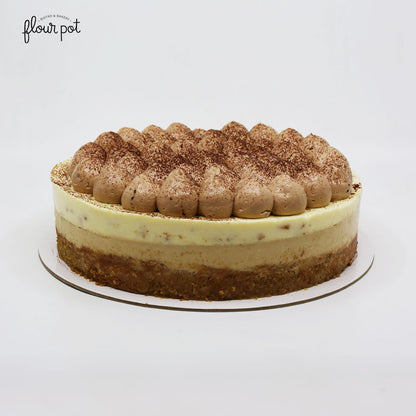 Layered banana fromage cake with a creamy mousse center, biscuit crust, and piped chocolate cream topping dusted with cocoa